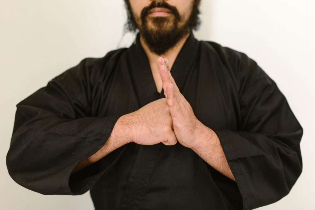 Close-up of a martial artist in a black gi performing a traditional hand salute against a neutral background.